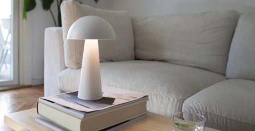 Ett soffbord med en vit bordslampa på ett par böcker ståendes bredvid en soffa.