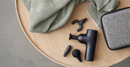 En svart massagepistol med tillbehör liggandes på ett runt träbord.