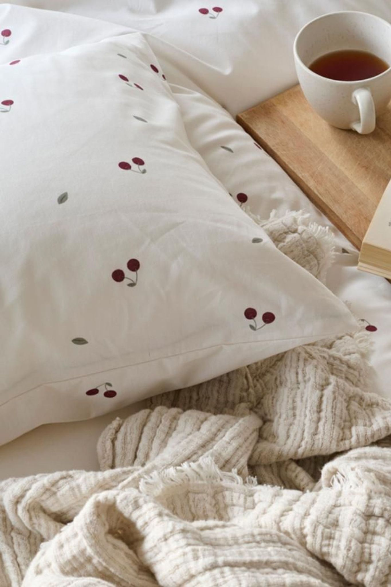 En kudde med små körsbär som motiv bredvid en frukostbricka med en kopp te