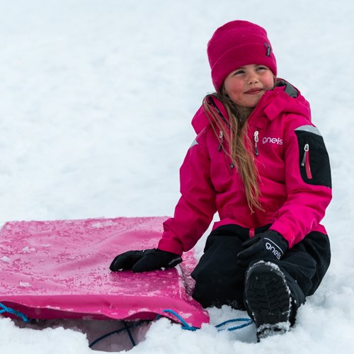 Gneis Supershape vinteroveral i cerice, vattentät, varm och smidig overall. Barn leker i snön med åkmadrass.