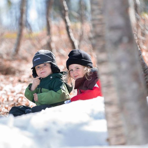 Gneis Minishape vinteroverall i grönt och rött, varm, mjuk och smidig overall. Två barn leker i snön.