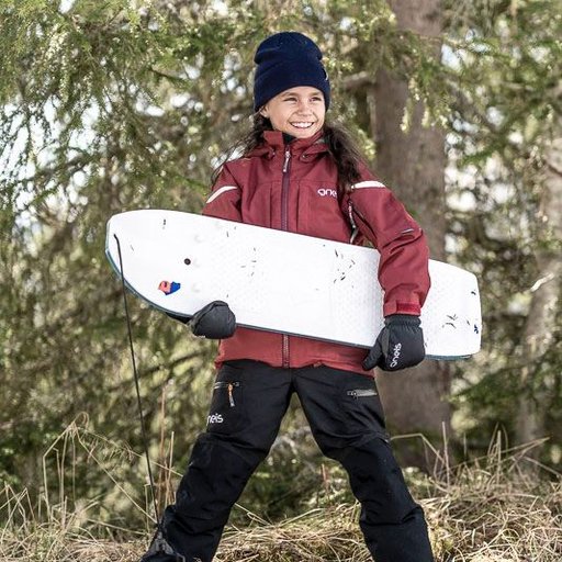 Gneis Thumb Pro tumvante. Varm, vattentät vinterhandske med bra grepp. Barn som står i torrt gräs med en snowboard i famnen.