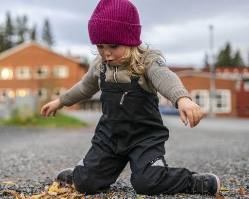 Ett litet barn som leker i sina slitstarka Granit Bib hängselbyxor som hon fått istället för galonbyxor.