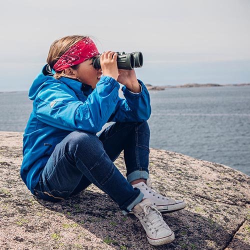 Barn sitter på klippa med kikare i Speed Shell skaljacka och Ossoami Amigo jeans från Gneis