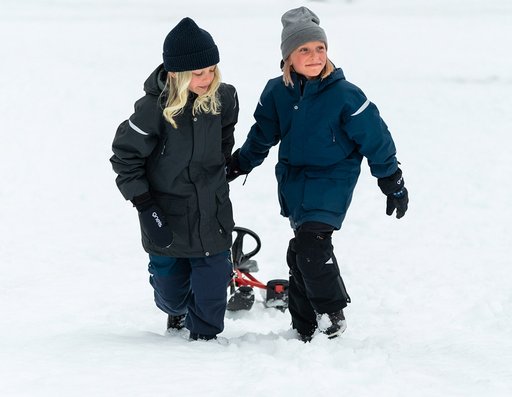 Två barn som drar en bob i snön iklädda Gneis vinterparkas