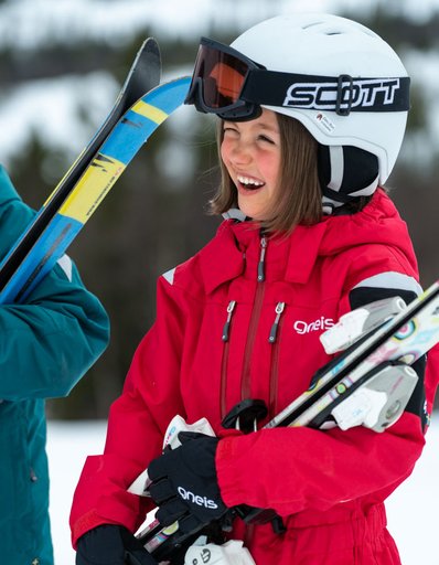 Flicka som bär på skidor klädd i en av Gneis alla skidjackor för barn