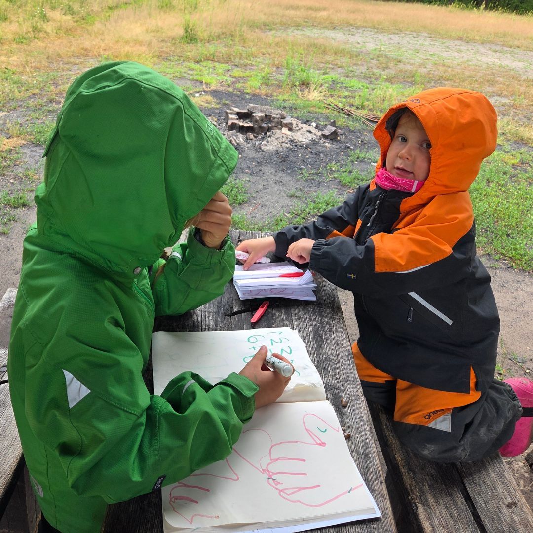 Två glada barn som ritar utomhus i Gneis skalkläder för barn