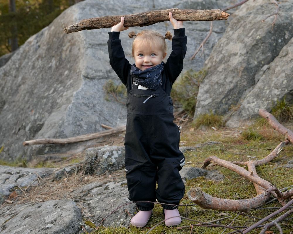 En flicka som har på sig skalbyxan Granit Bib från Gneis barnkläder – den slitstarka ersättaren till galonbyxan