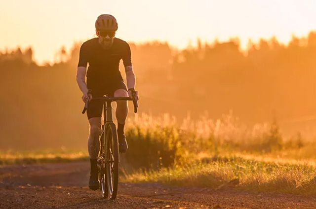 Pyöräilijä ajaa Nuroad gravel-pyörällä soratiellä auringonlaskussa