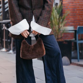 Kvinne med blazer, hvit skjorte og brun håndveske i fuskepels