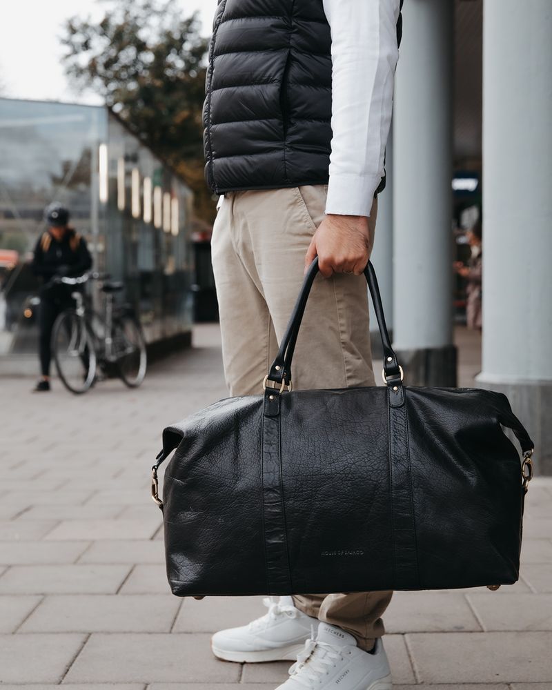 Mann med jeans holder en brun skinnbag inne på et bibliotek
