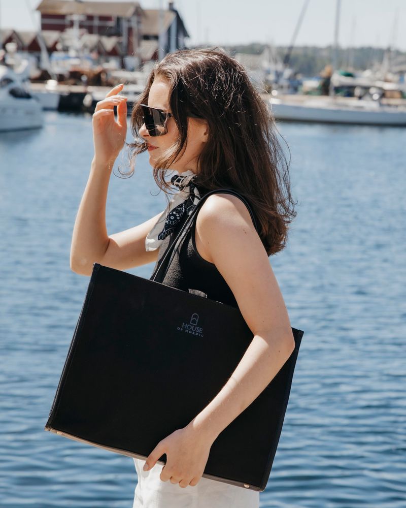 dame ute ved sjøen med en stor sort totebag
