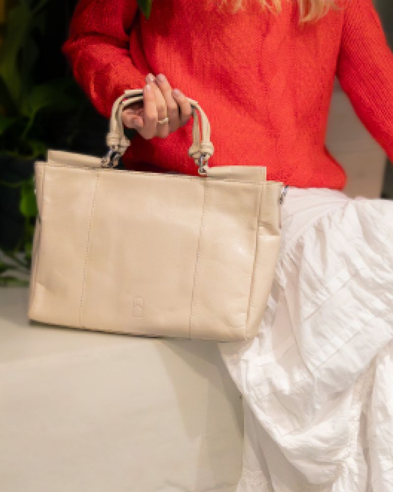 Beige handbag House of Nordic hold av dame i rød genser og hvitt skjørt