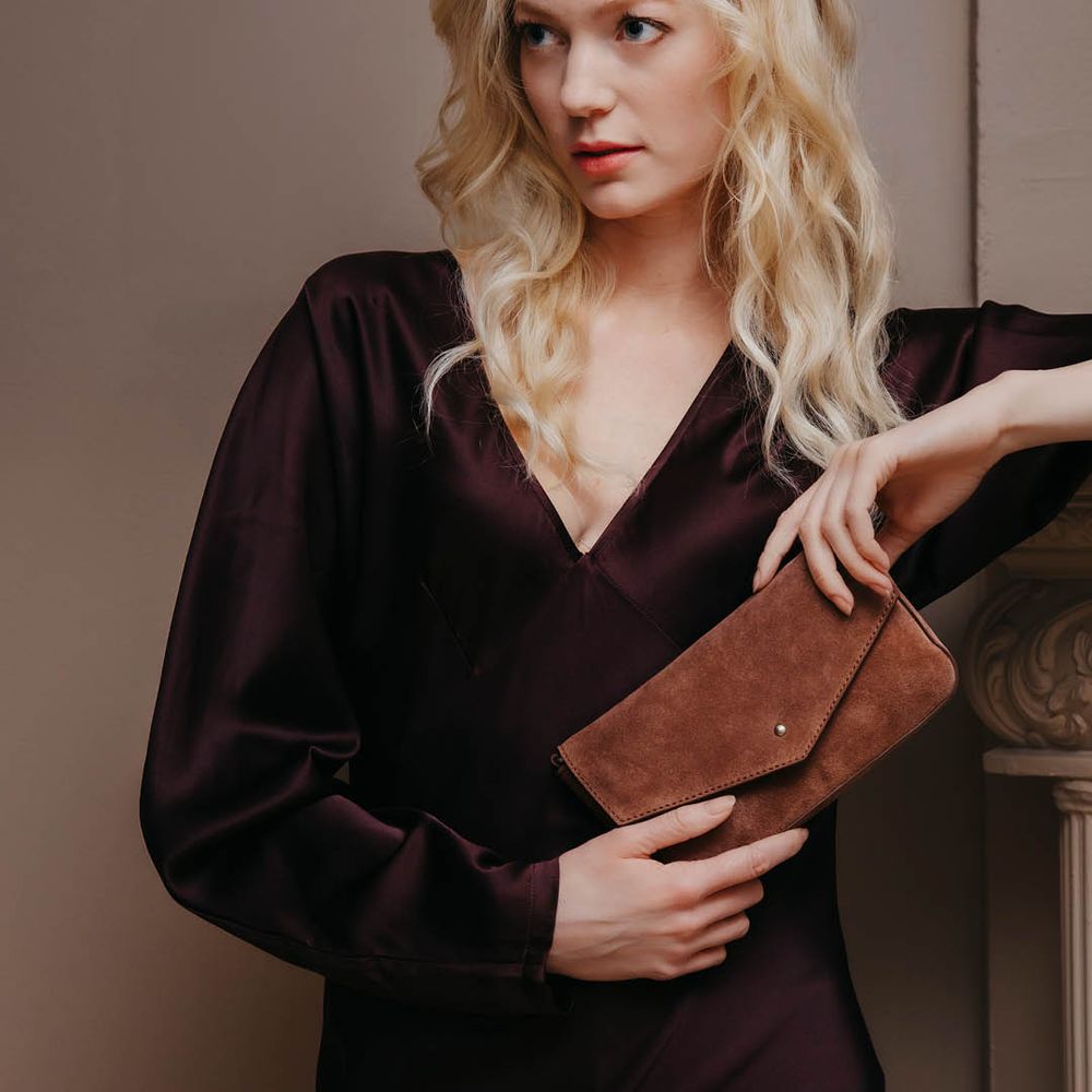 Clutchveske i semsket skinn holdt av blond dame i elegant antrekk