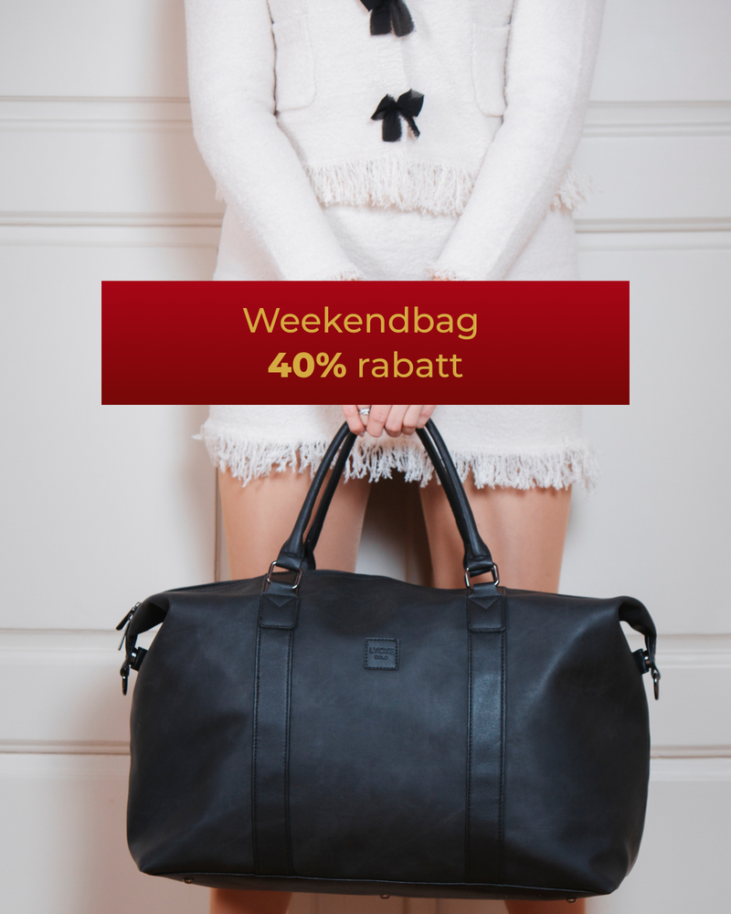 svart weekendbag holdt av dame i vite klær. serien kim 40% rabatt.