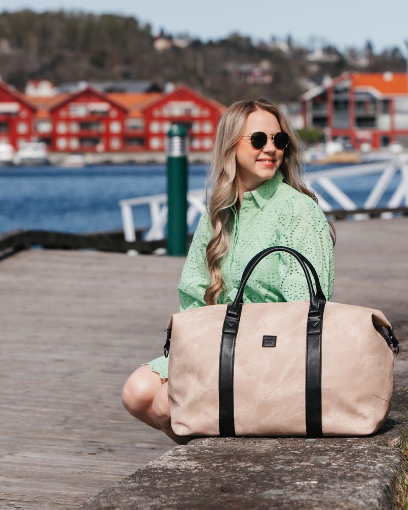 beige wekkendbag ved siden av dame i grønn kjole med vann i bakgrunn