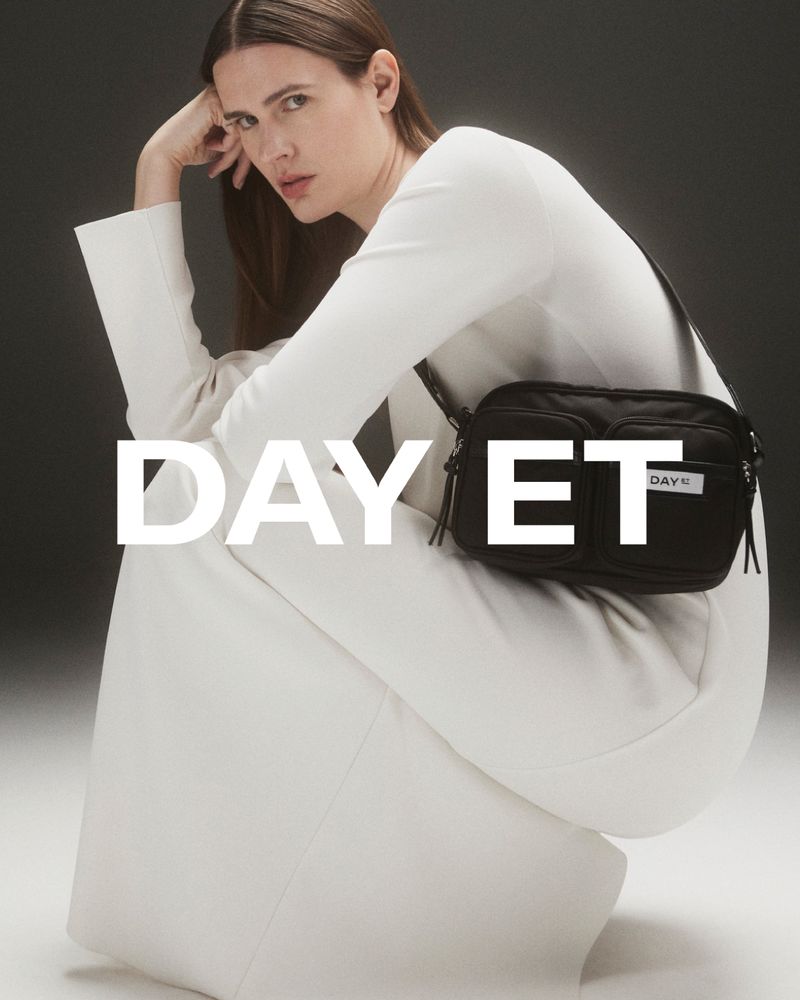Kvinne med brunt hår, hvit kjole og svart Day Et veske