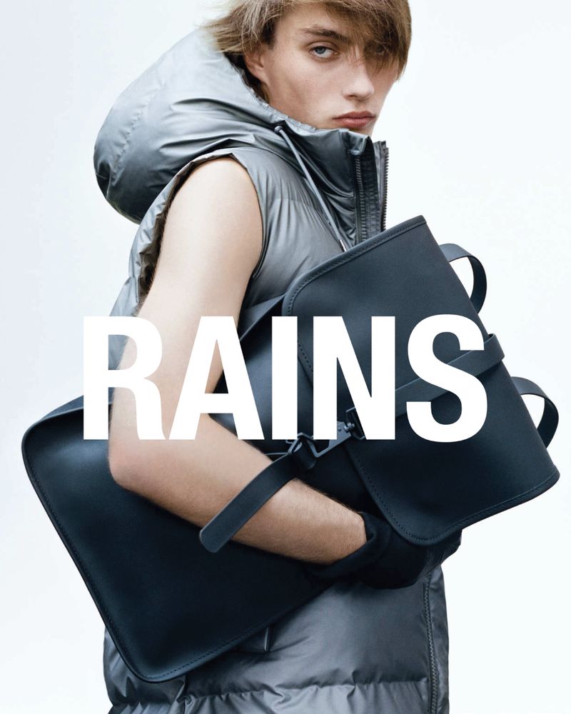 Androgyn modell i grå vest med svart Rains ryggsekk