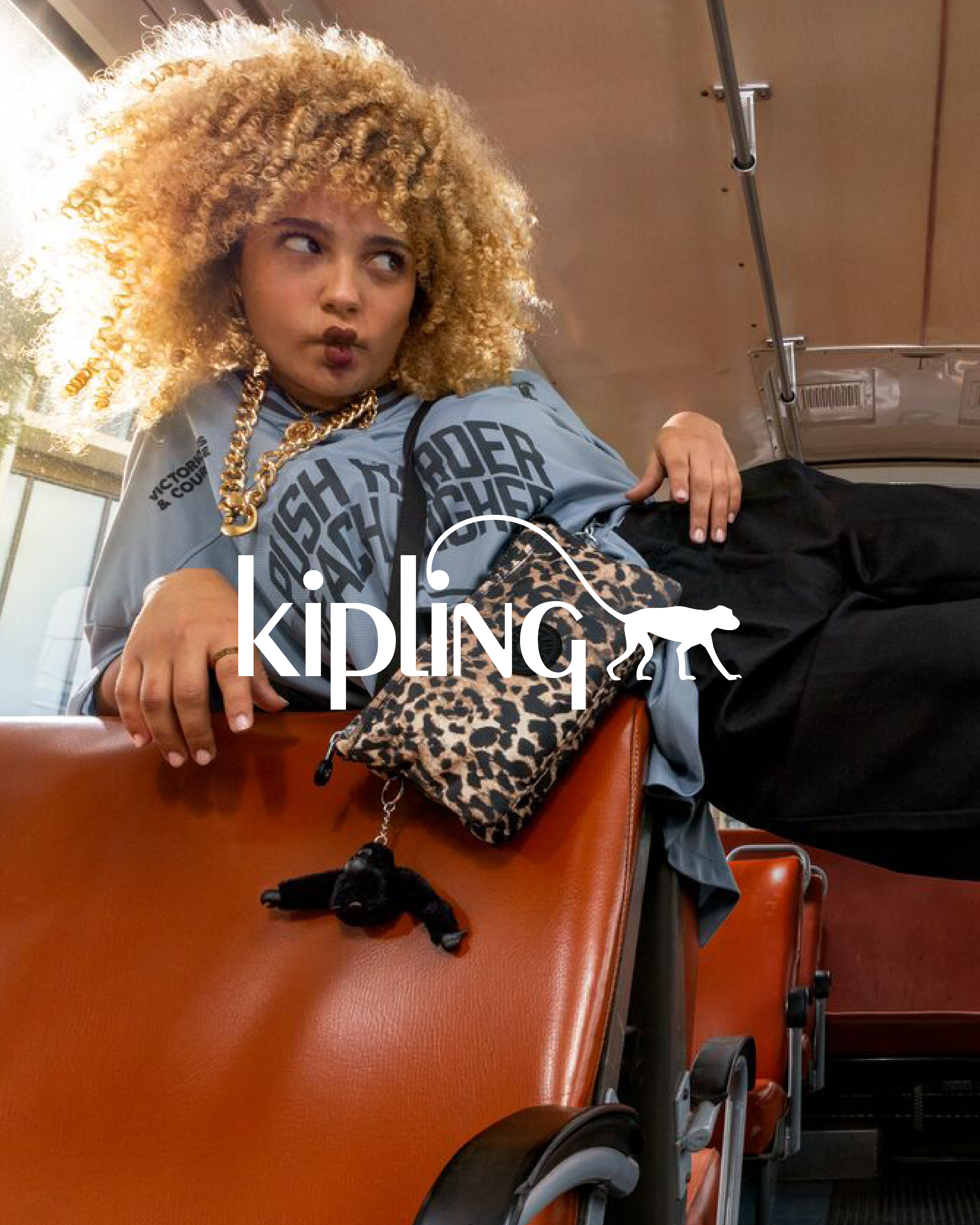 dame som ligger skrått i buss med liten leopard veske, kipling logo