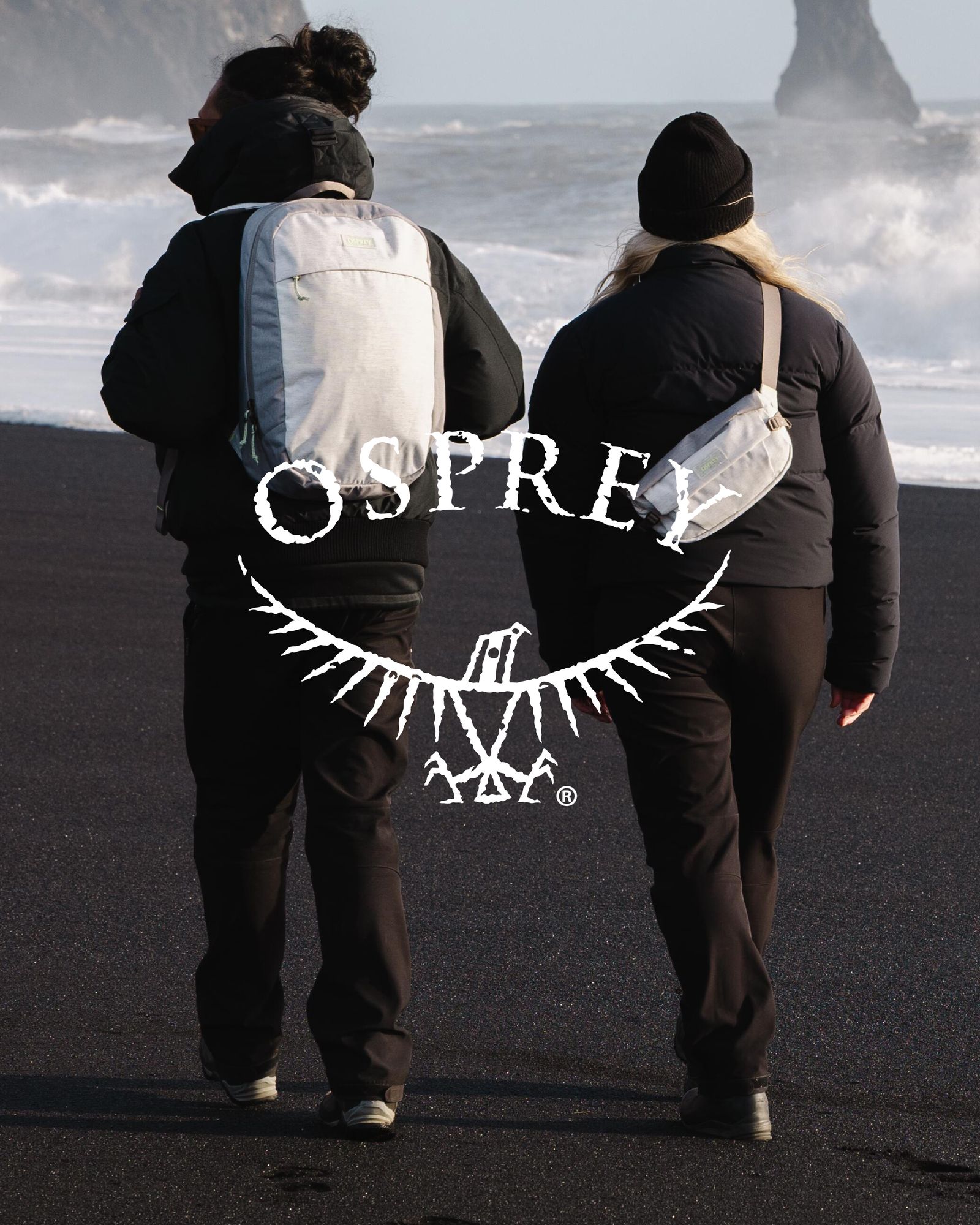 Et par i sorte klær på strand med lysegrå Osprey sekk og osprey logo
