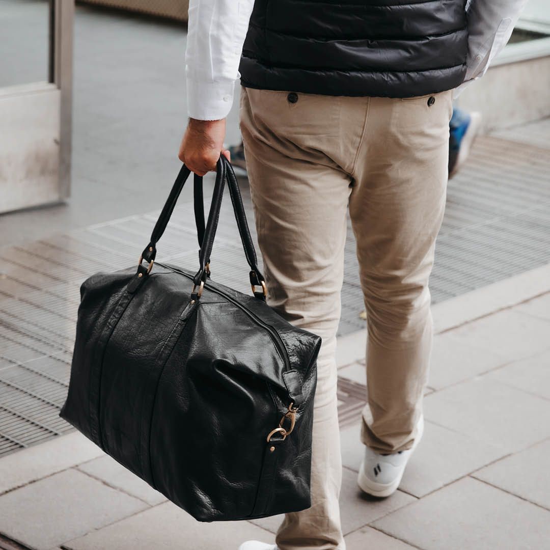 Weekendbag i skinn båret i hånden av person i bymiljø