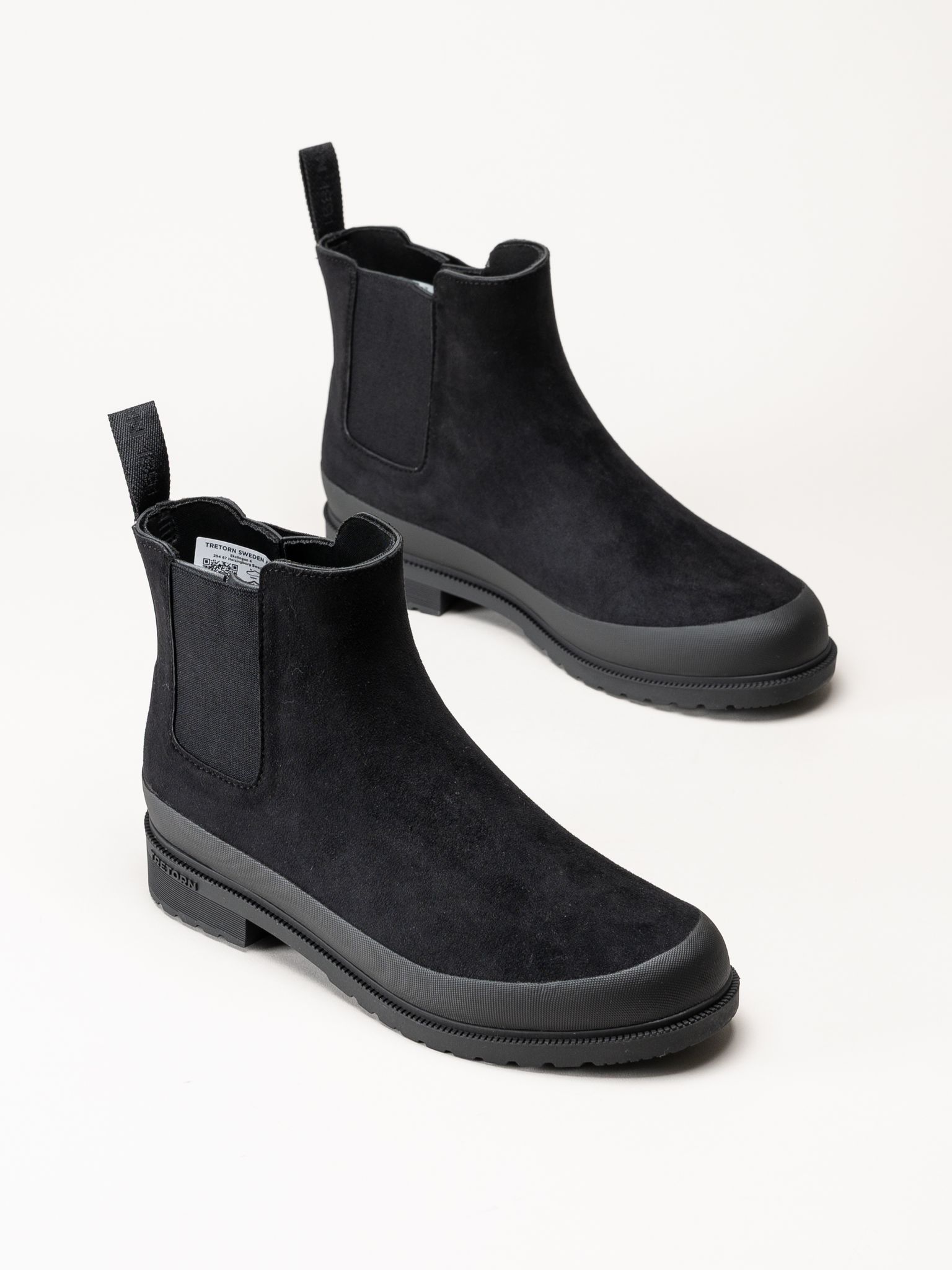 Ett par svarta Chelsea-boots i mocka med dragöglor och gummisulor