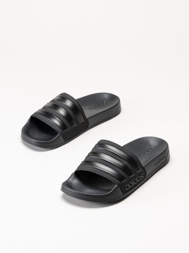 Ett par svarta Adidas-badtofflor med tre ränder