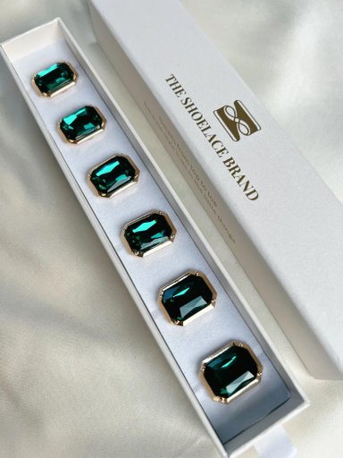 Sex smaragdgröna skoklämmor med juveler i en vit ask