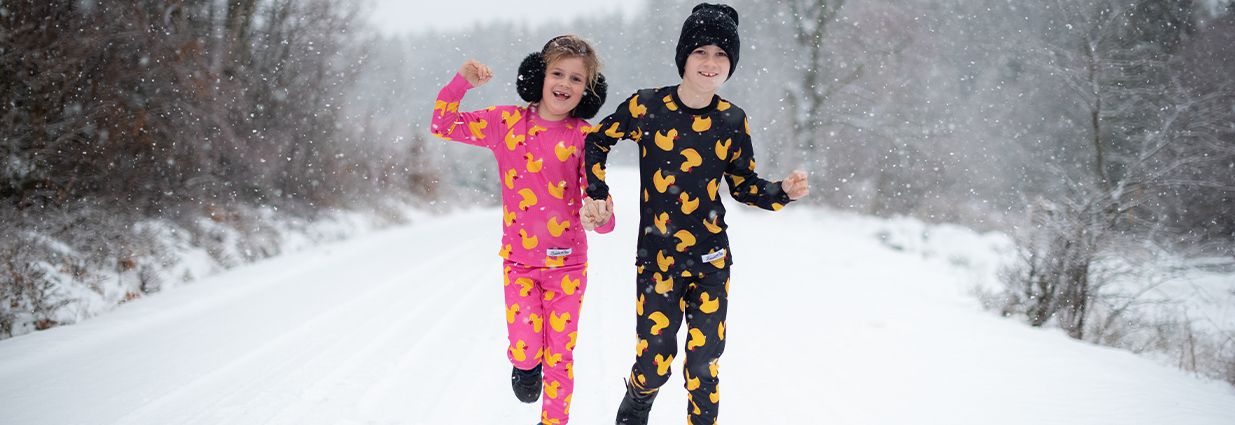 Två barn/ juniorer springer i snön med underställ ifrån Blount & pool som är rosa och svarta med gula ankor på 