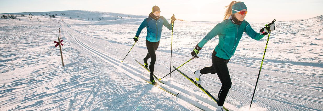 Två personer som åker längdskidor med varma och sportiga längdskidåkningskläder