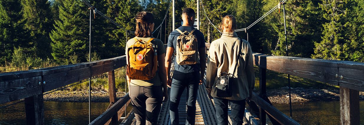 Tre personer som går på en bro med ryggsekker fra Fjällräven
