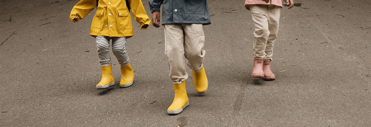 Tre barn/juniorer som er ute og går med gummistøvler i fargene gul og rosa