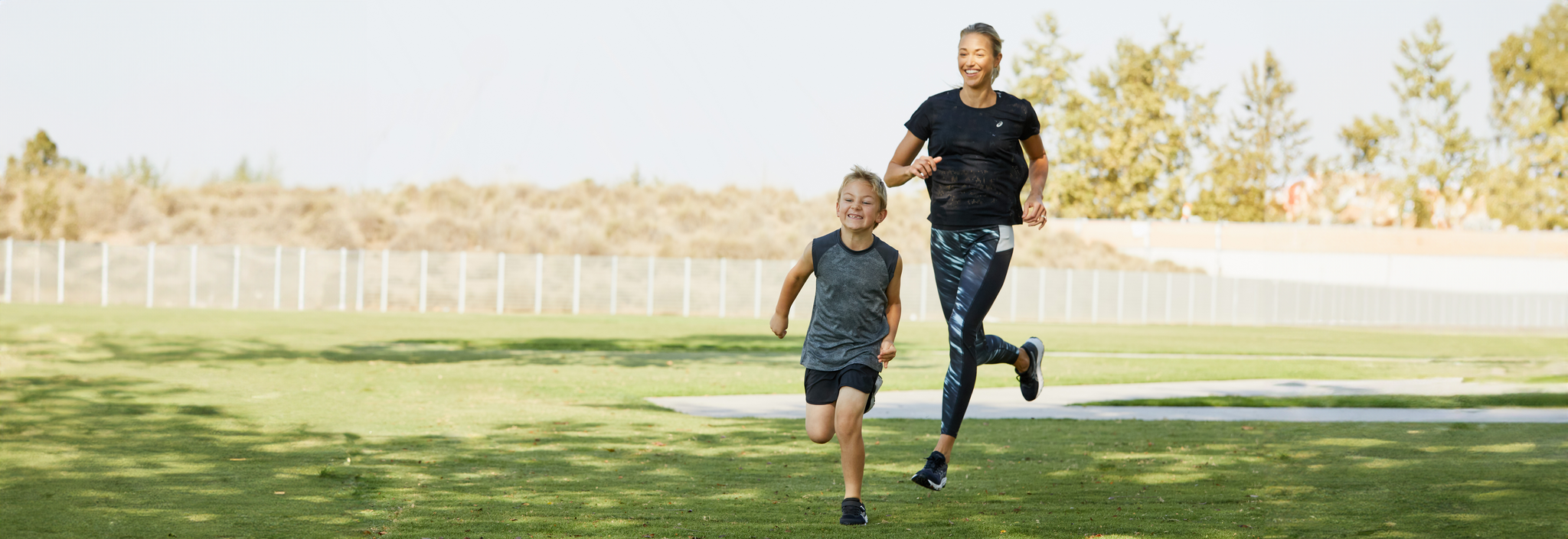 Äiti ja lapsi juoksevat nurmikentällä urheiluvaatteet päällä