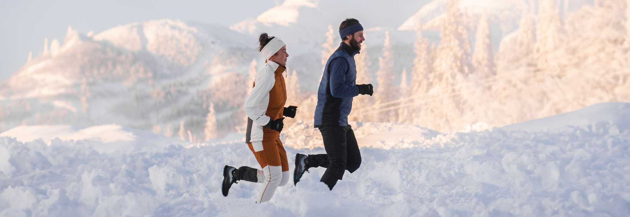 Mies ja nainen juoksemassa talvella lumisessa tunturimaisemassa.