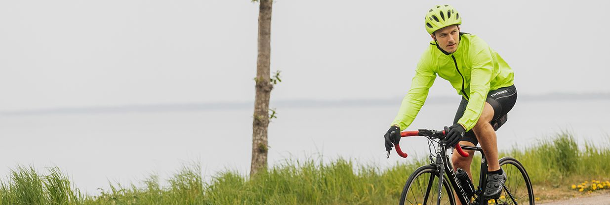 En fyr som sykler med en limegrønn sykkeljakke og et par svarte sykkeltights fra Swedemount