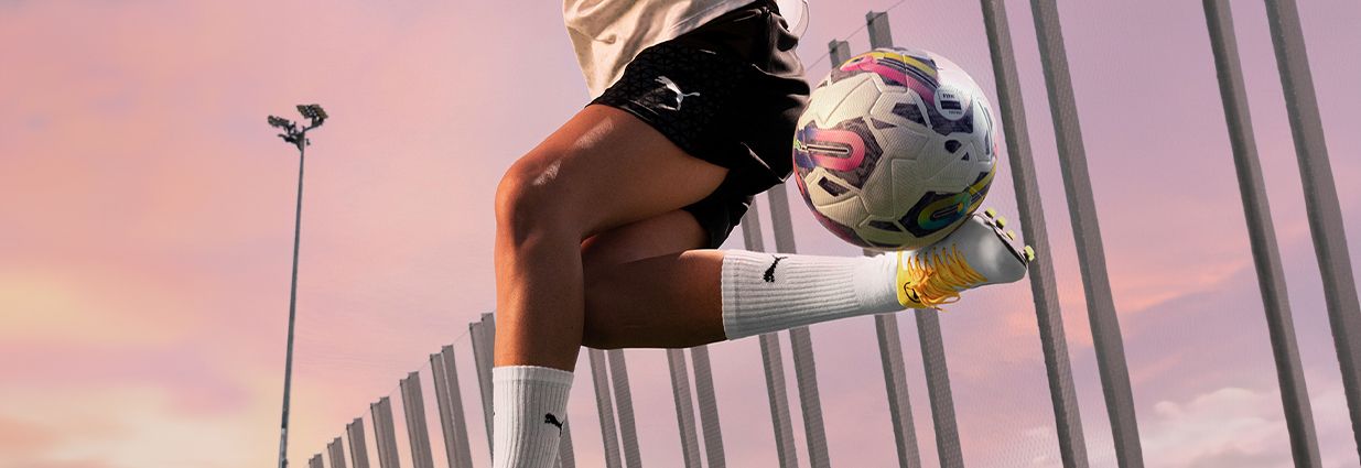 Jalkapalloilija kikkailee jalkapallon kanssa Puman shortsit ja valkoiset sukat jalassa.