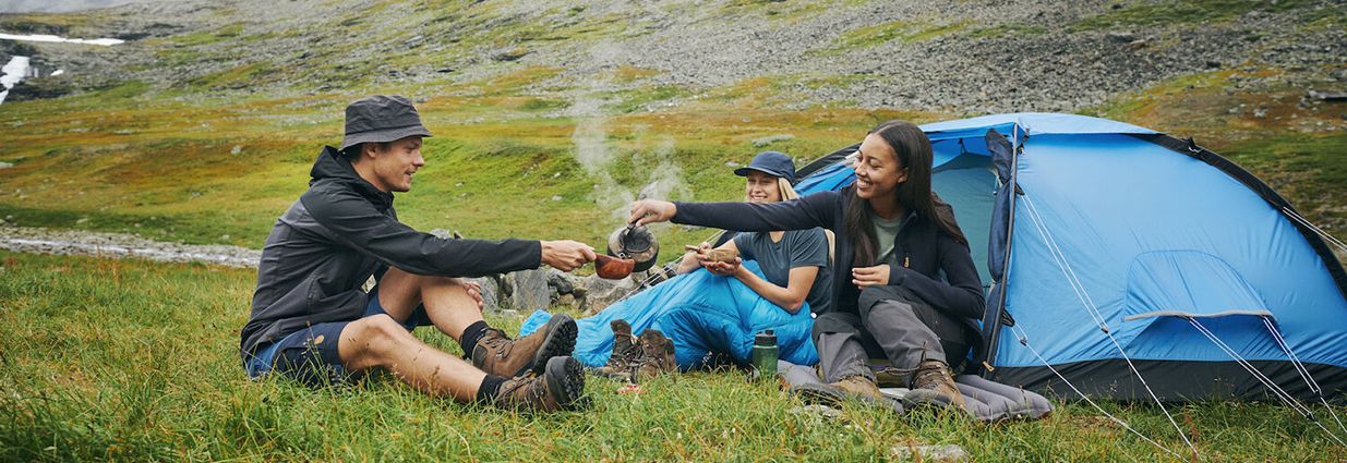 En kille och två tjejer som dricker kaffe vid sin campingplats