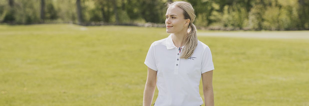 En tjej som går på en golfbana i en vit piké från Swedemount 