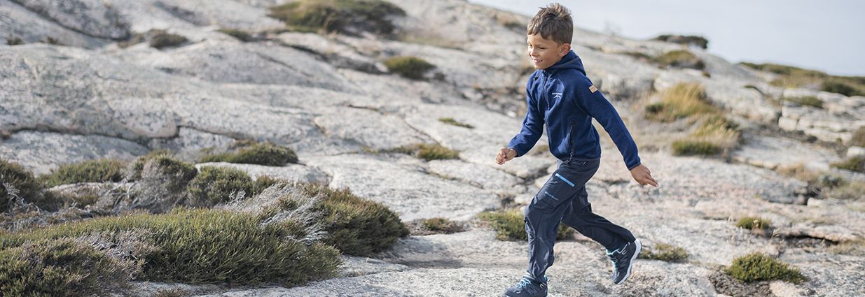 Et barn/junior som er ute i naturen og løper med aktivitetstøy i form av en fleece topp fra Swedemount og en funksjonsbukse