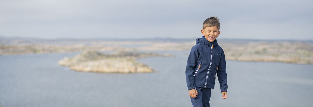 Ett barn som är ute och går vid havet i en jacka och byxa från Swedemount