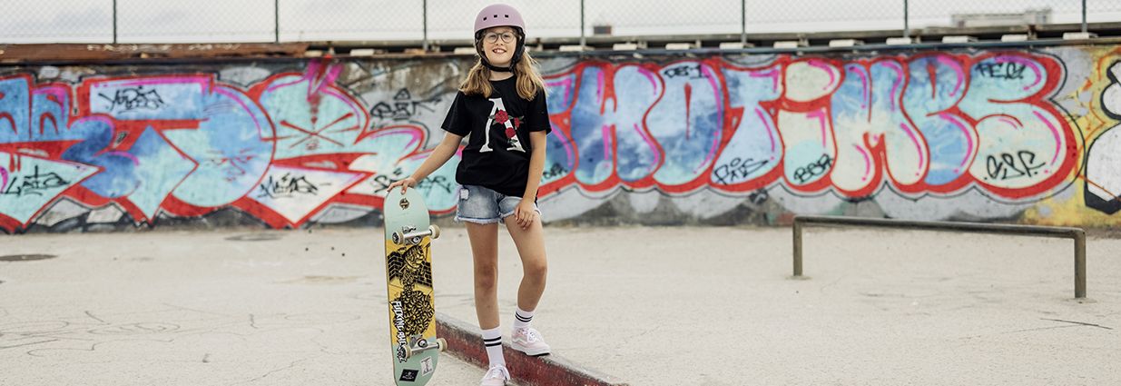 En tjej som står och håller i en skateboard i en skatepark med en t-shirt från Slade