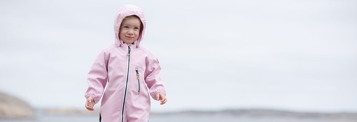 Två barn/ juniorer som åker pulka i snön med rosa och blåa vintriga overaller ifrån märket Swedemount