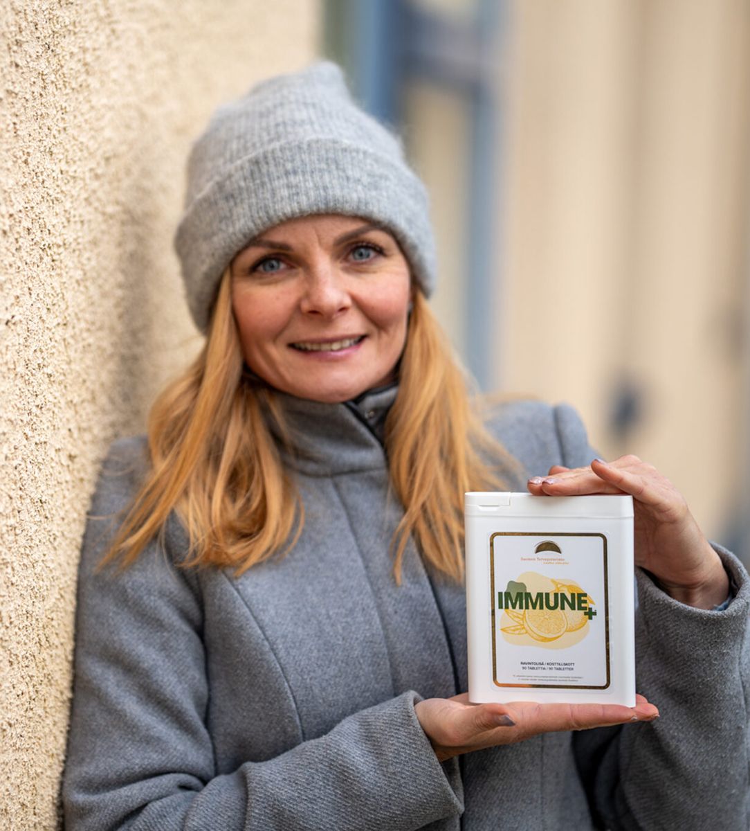 Woman in a grey coat and beanie holding an Immune+ supplement container