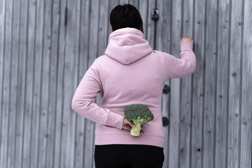 woman holding a broccoli behind her back